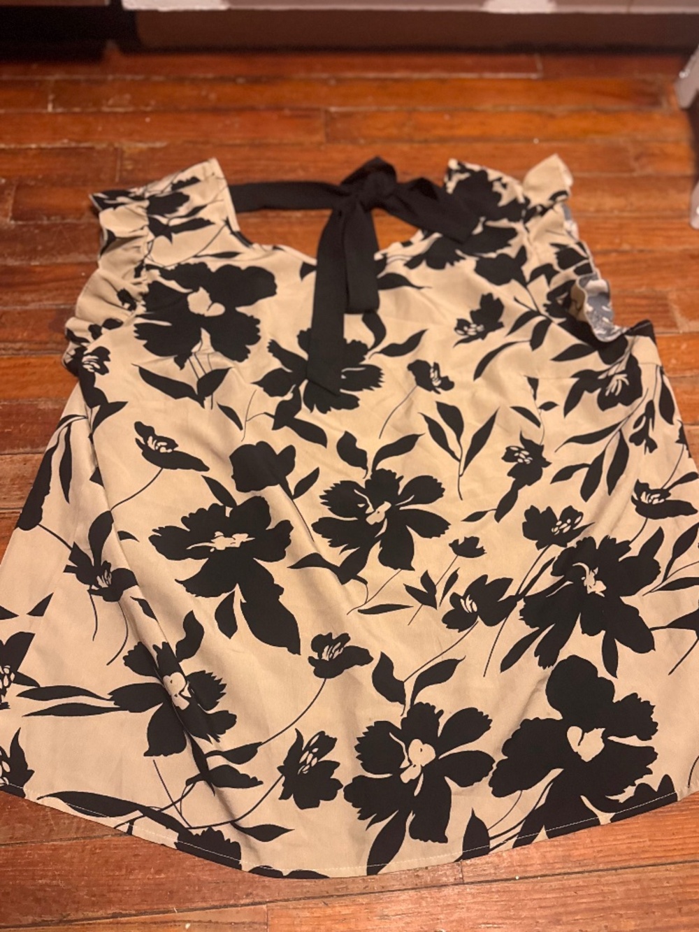 Sleeveless blouse with ruffle shoulders. Black floral print on a cream backgroun